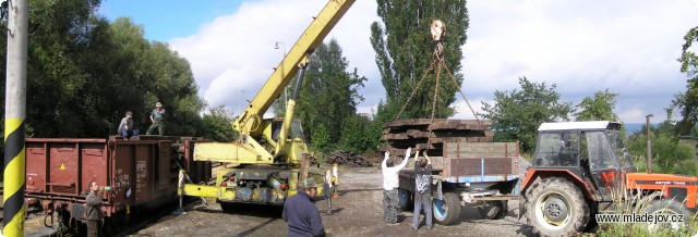 Fotografie Celkový pohled na překládku pražců z&nbsp;železnice na silnici na skládané fotografii pořízené z&nbsp;rampy mladějovského složiště. 
