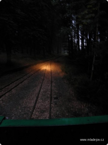 Fotografie Pohled z&nbsp;lokomotivy v&nbsp;čele nočního vlaku na reflektorem osvětlenou trať úzkorozchodné dráhy.
