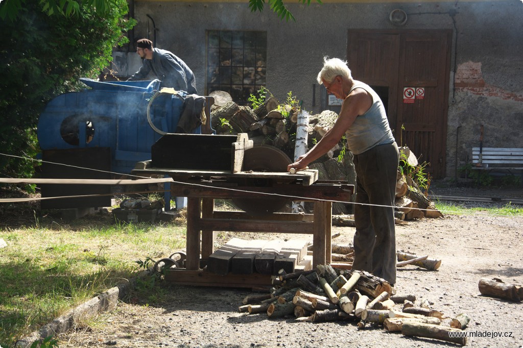 Fotografie S ukázkou činnosti stabilního motoru běží i předvádění transmisní okružní pily v&nbsp;provozu. Pozitivním vedlejším efektem je pěkná hromádka nařezaného dřeva.